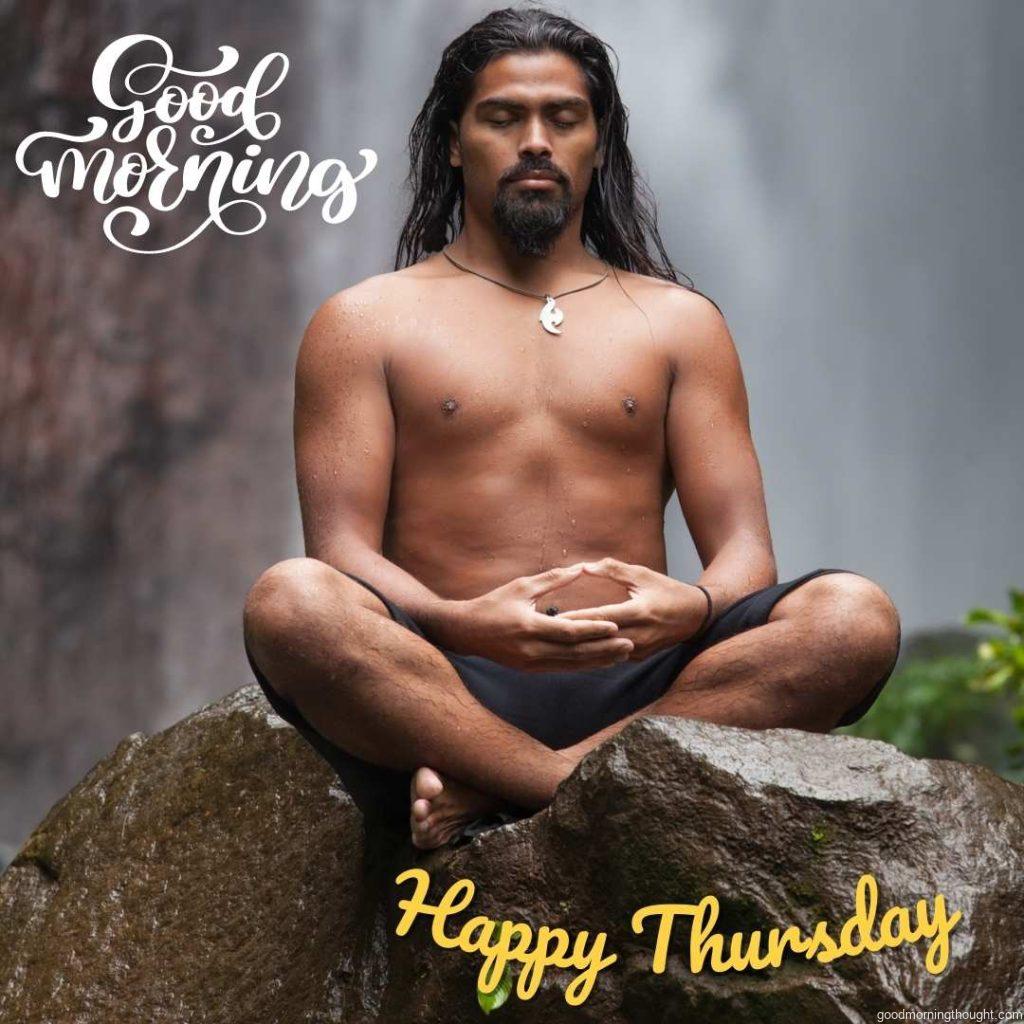 A man sits in meditation on a rock at a waterfall in a tropical rainforest. _Good Morning, Happy Thursday_ text