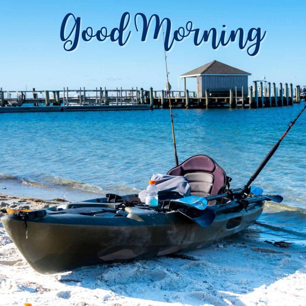 Fishing kayak with equipment stowed on a beached sandy shore with a long pier over ocean water in the background. God morning beach image