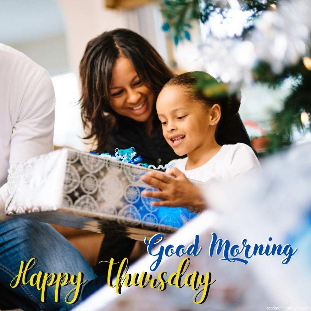 Mother and daughter open presents under the Christmas tree with a _Good Morning, Happy Thursday_ text