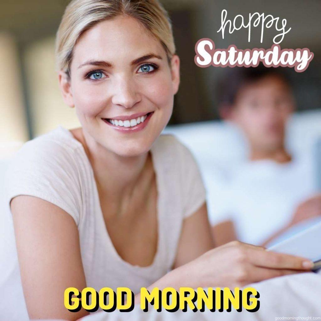 Shot of a happy young woman lying in bed and reading a magazine with her husband in the background with the _Good Morning, Happy Saturday_ text