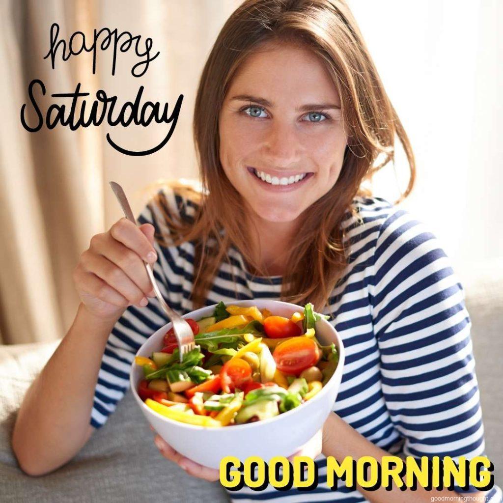 Shot of a young woman eating a bowl full of salad on her sofa at home with the _Good Morning, Happy Saturday_ text