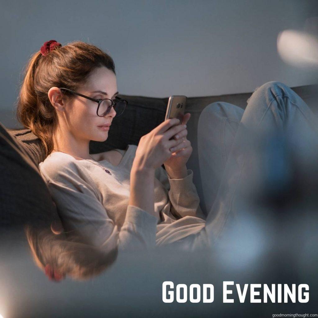 A close-up of a beautiful woman wearing glasses in the evening relaxing with her smart phone with a _Good Evening_ text