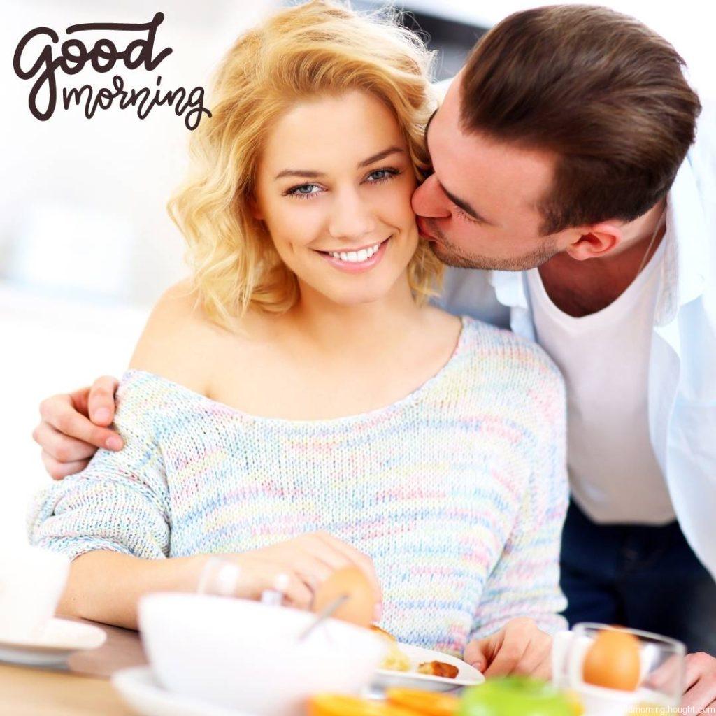 A picture of a young man giving a good morning kiss to his wife in the kitchen