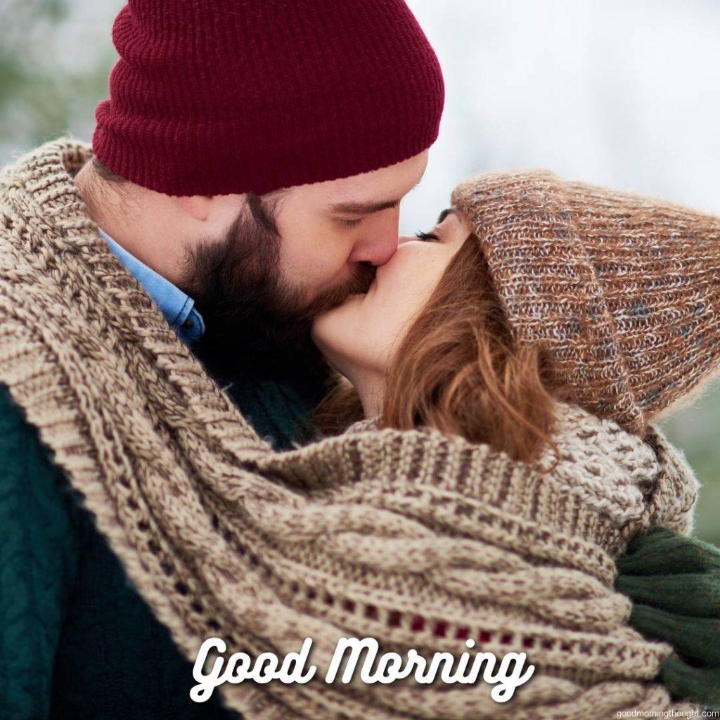 Lovely young couple wrapped in a warm knitted scarf standing outdoors and kissing, they wearing hats and sweaters. Good Morning Image