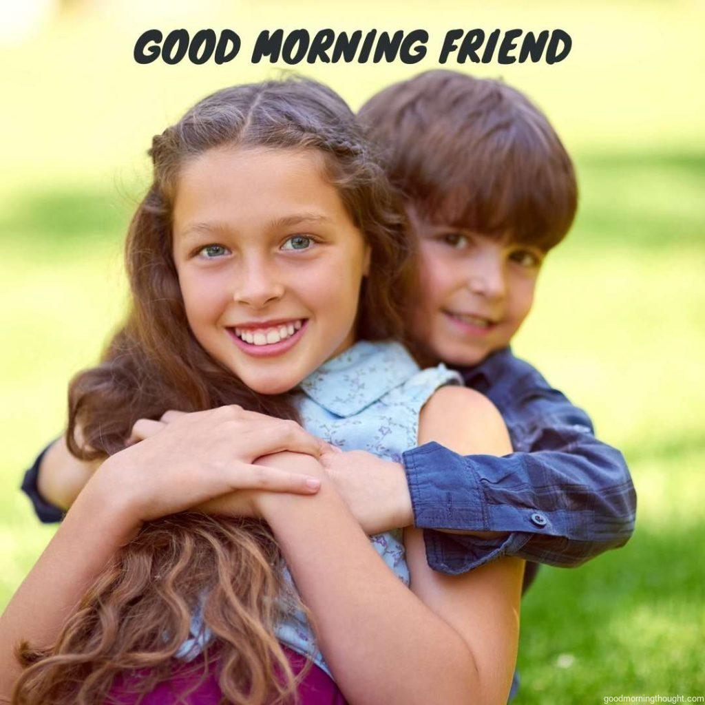 Portrait of a young boy embracing his girl friend while sitting on the grass outside, Good morning text