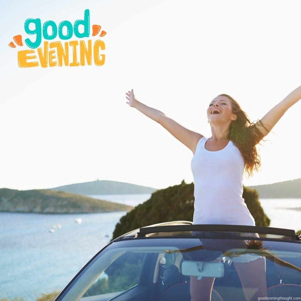 Shot of an attractive young woman standing with her hands raised from the inside of her convertible with _Good Evening_ text