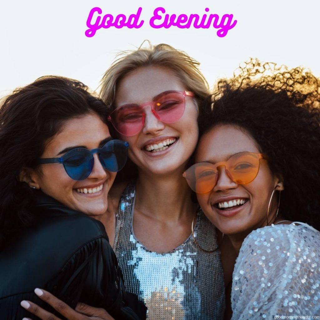 Three happy women wearing sunglasses hugging at evening outdoors with _Good Evening_ text