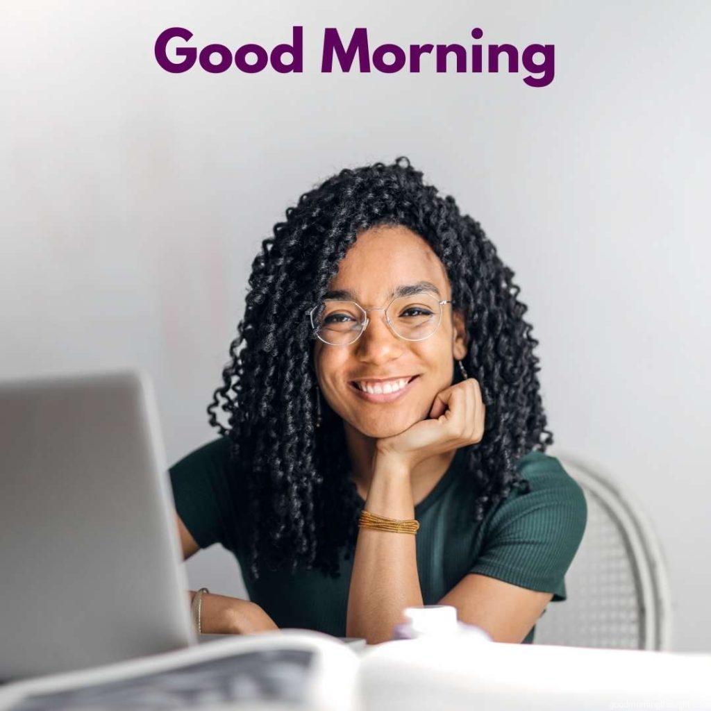 A happy ethnic woman sits at a table with a laptop. _Good Morning_ text. Happy Good Morning Images