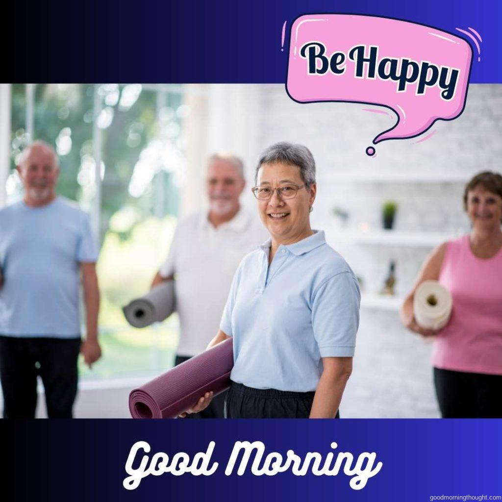 A multi-ethnic group of happy adult men and women are indoors in a fitness studio. They are holding exercise mats and smiling at the camera. Word Good Morning