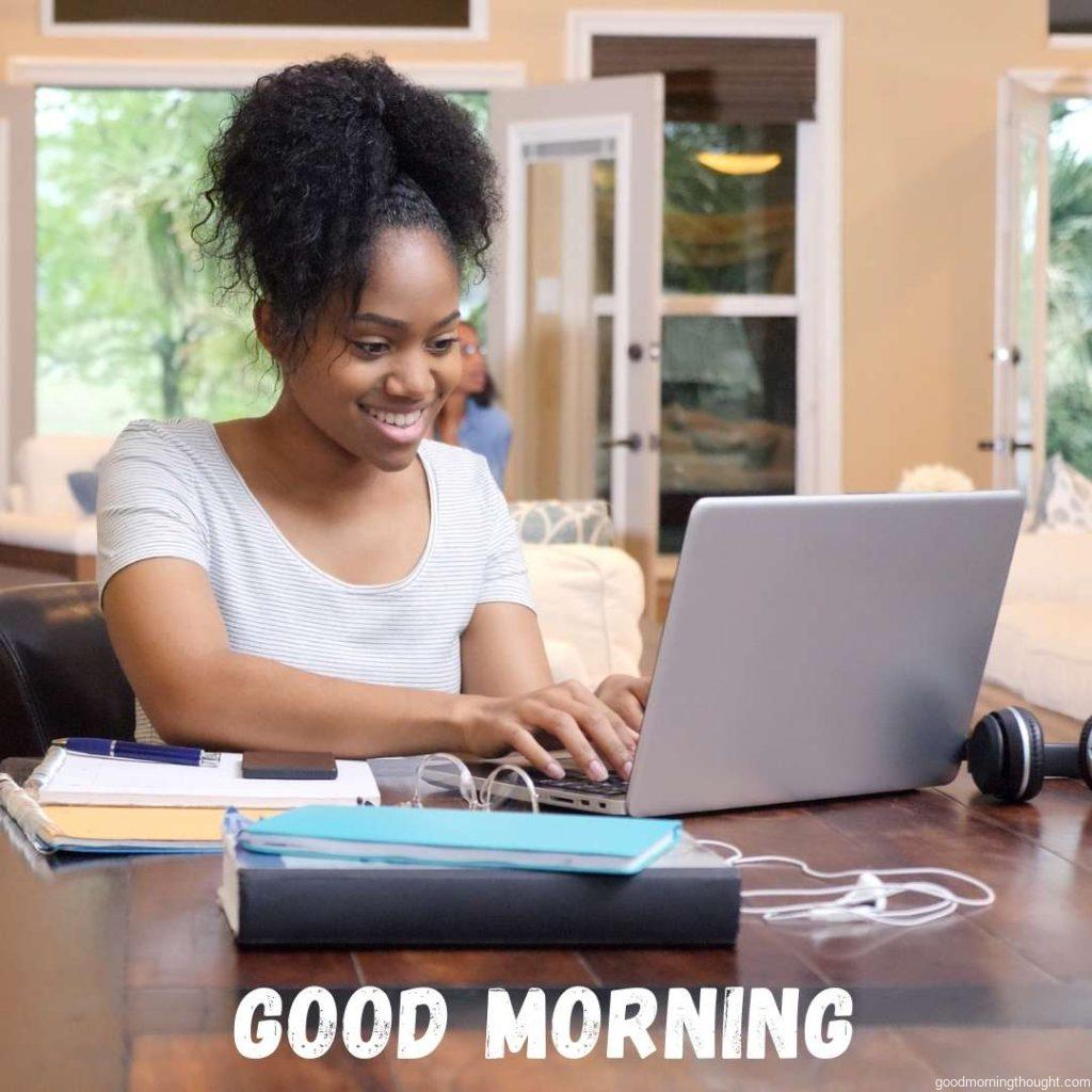 An African American young adult works on a report for school at the dining room table while her mother looks out of the living room window. Good Morning Text