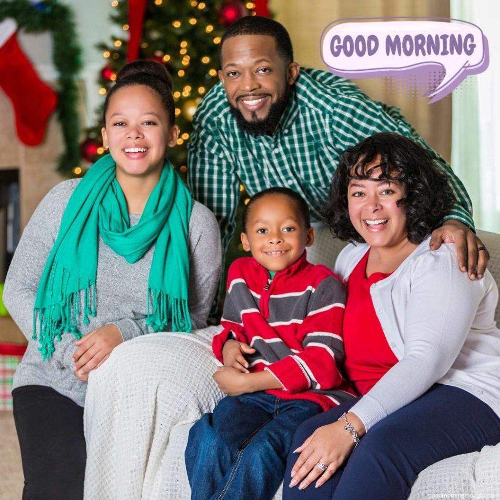 Beautiful African American families enjoy one another during the Christmas season. A lit Christmas tree, fireplace, and socks are in the background. Good Morning Text