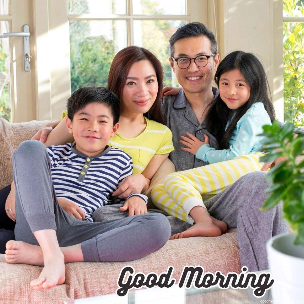 Happy family. A family of four sits on a sofa. They are all in their pyjamas, smiling and looking at the camera. Happy Good Morning Images