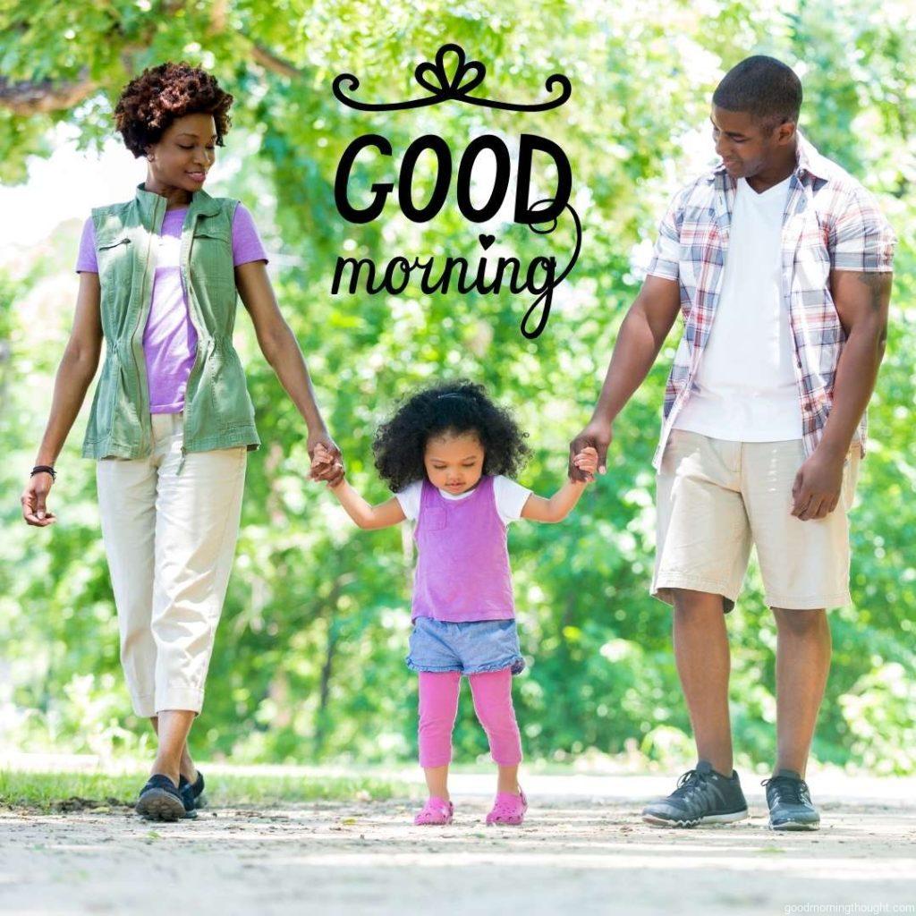 Loving African American mid-adult parents tenderly hold their toddler daughter's hands as they walk down a path in the park. African American Good Morning Images