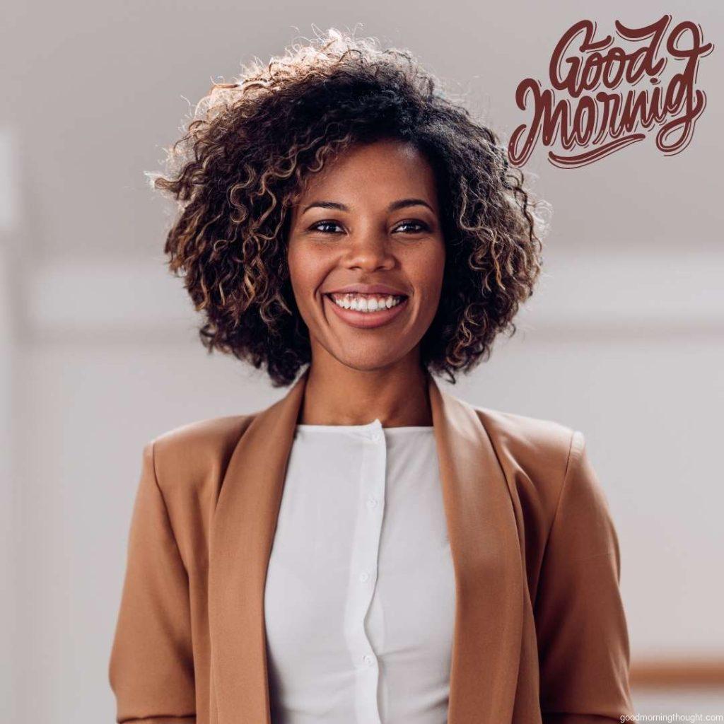 Portrait of a young, cheerful African American woman wearing a brown suit, smiling and looking at the camera Good Morning text