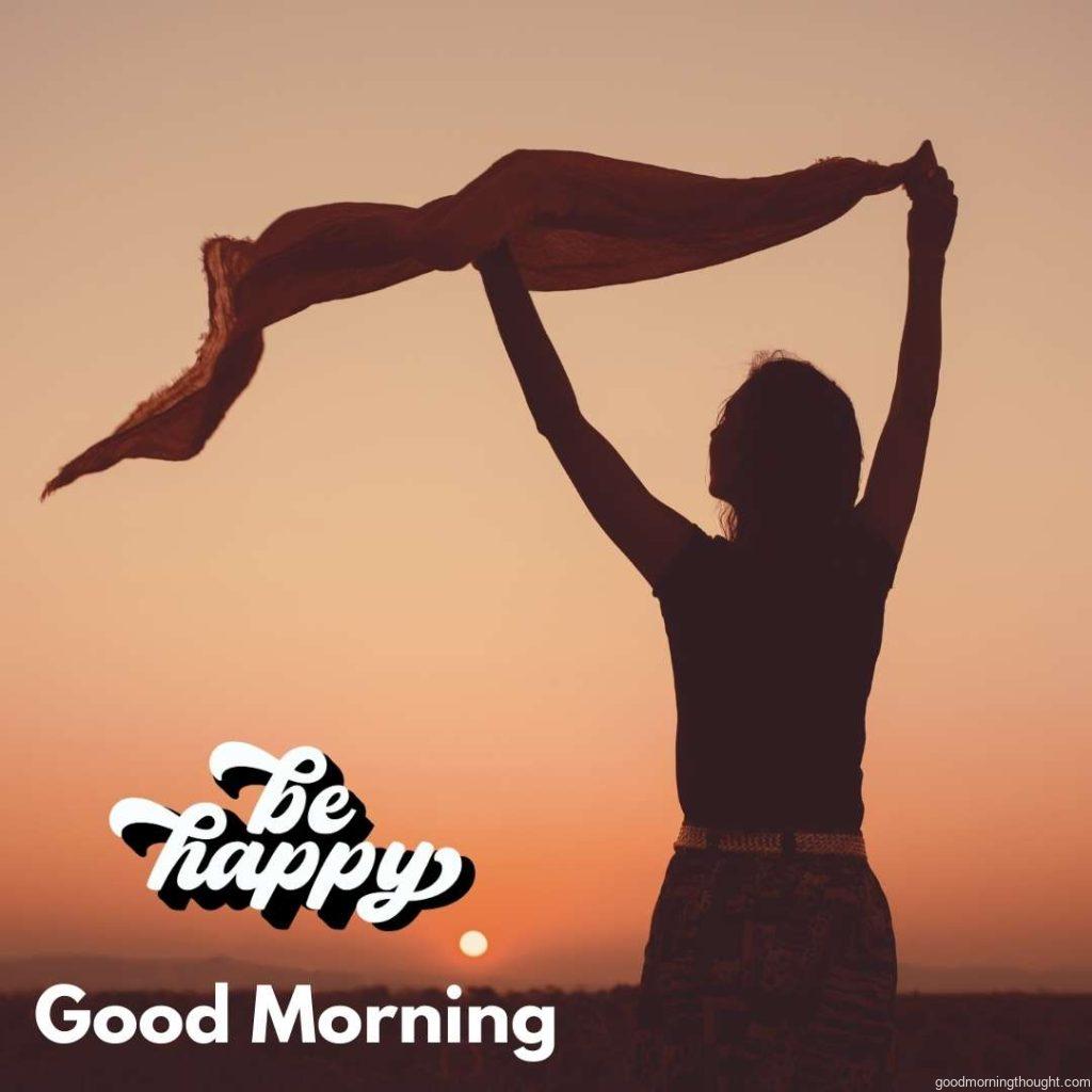 Rear view of a woman holding a scarf in the wind and enjoying a beautiful sunset, _Good Morning_ text